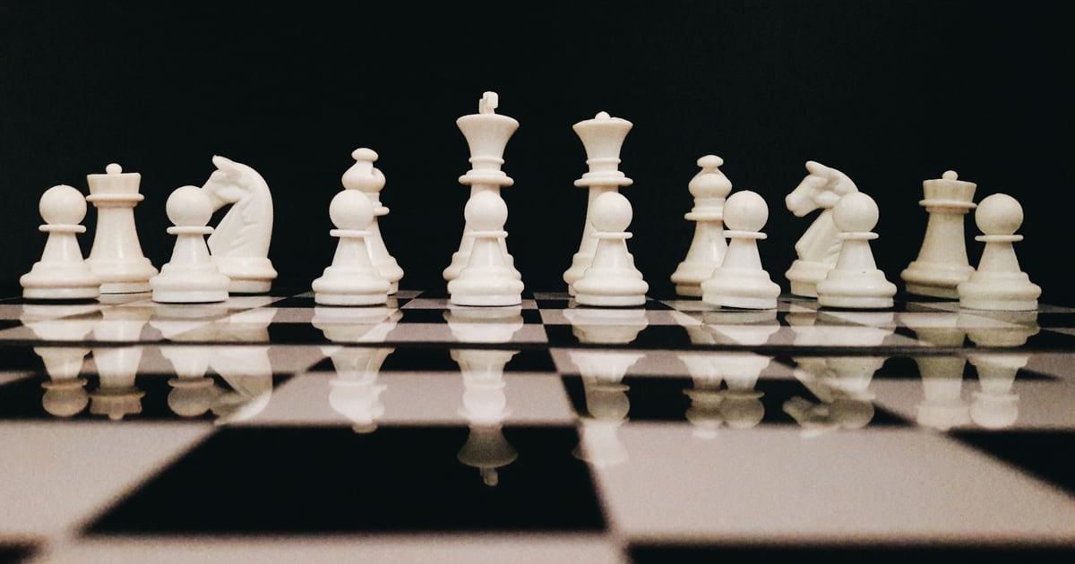 White chess pieces standing in an even row on a glossy black and white board