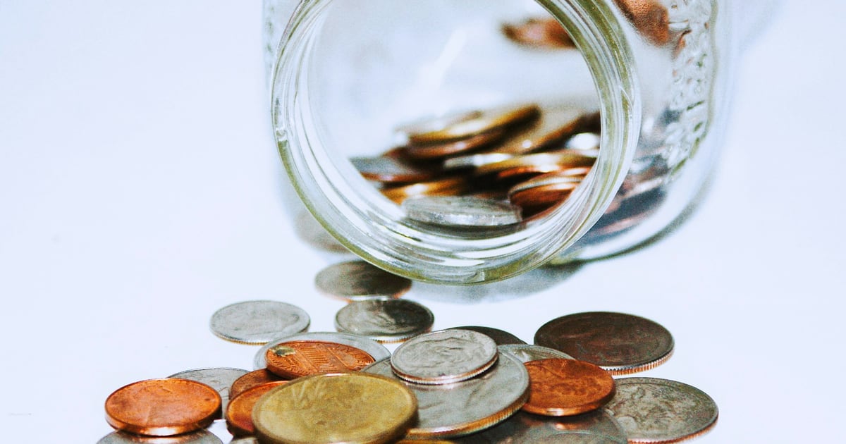 A tipped glass jar spilling copper and silver coins onto a white surface