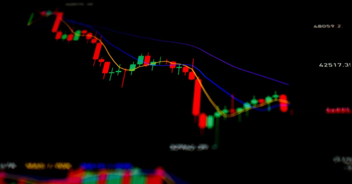 A candlestick price chart on a dark screen, falling in red candles before a partial recovery