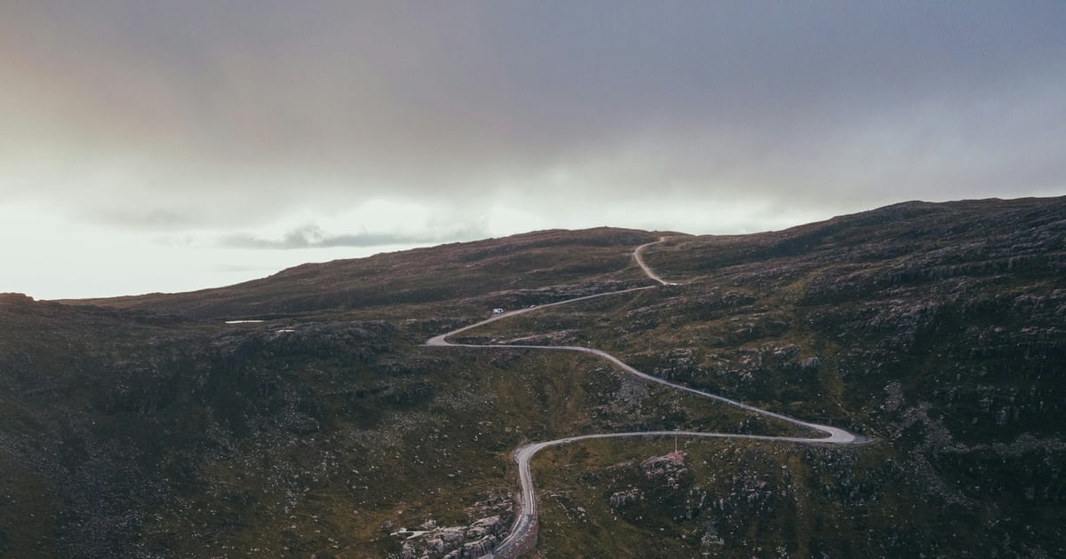 A narrow road snaking across dark moorland toward a ridge under an overcast sky
