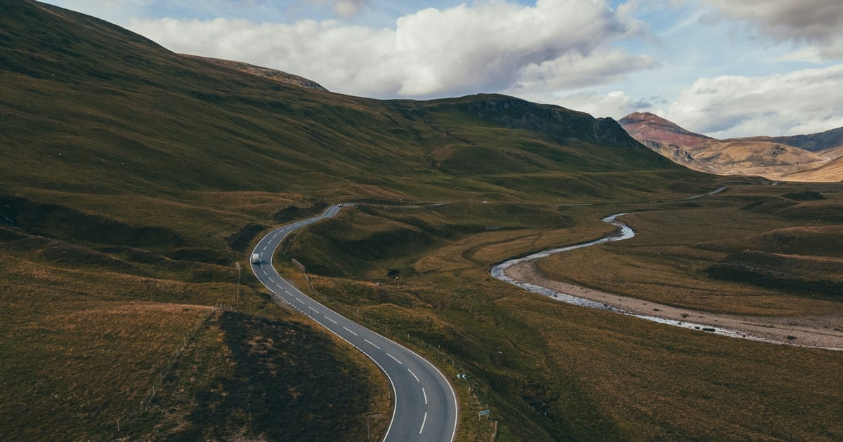 A long road winding through open hills, seen from high enough to follow its whole route