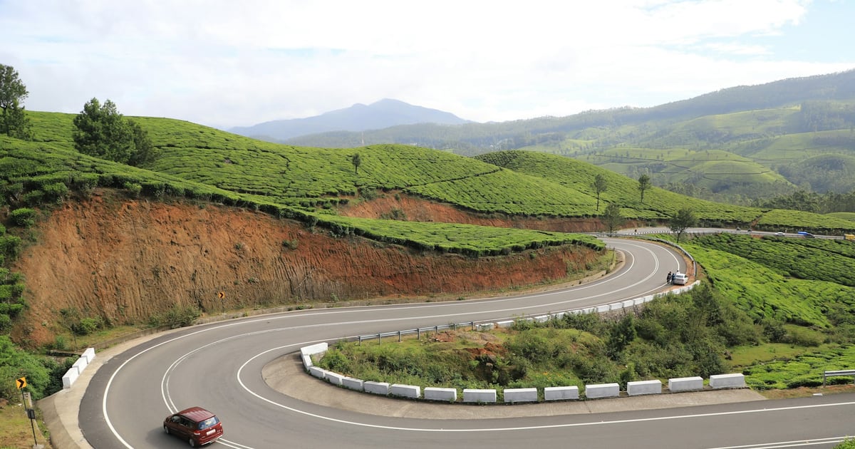 A single red car taking a wide hairpin bend on a hillside road through green fields