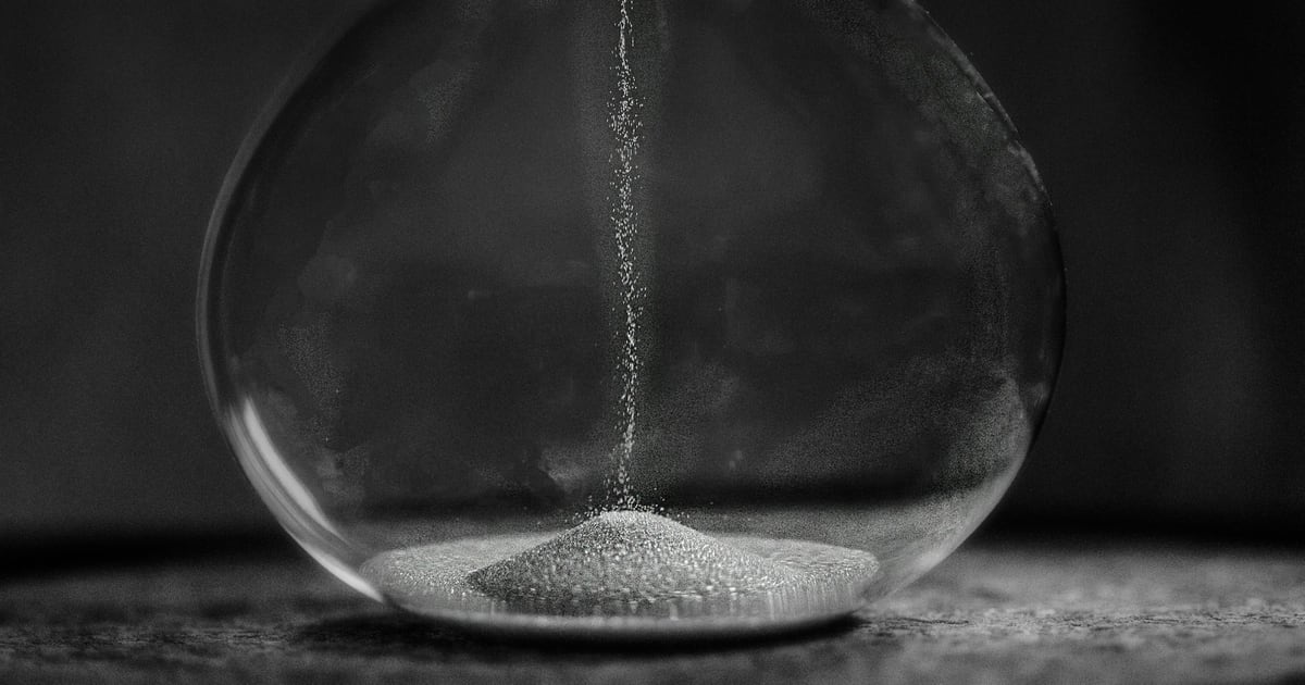 Close-up of an hourglass in black and white, a thin stream of sand falling into the lower bulb