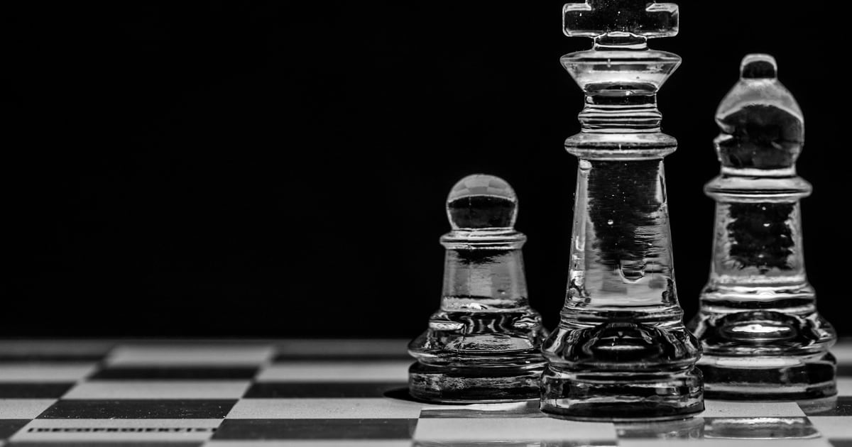 Three glass chess pieces standing apart at the edge of a board on a black background