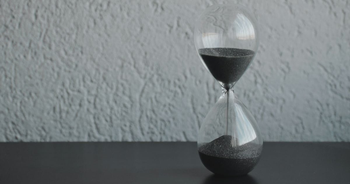 A small hourglass against a textured grey wall, sand running into the lower bulb
